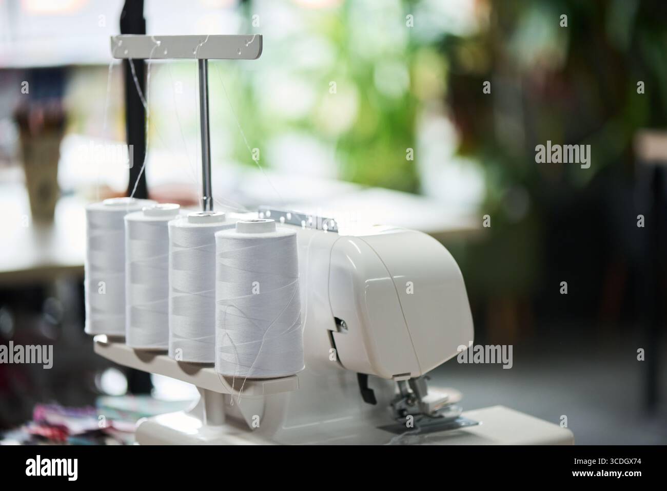 Industrial overlock sewing machine standing on table with multiple large thread spools attached, threads running through guides, blurred workspace background visible Stock Photo