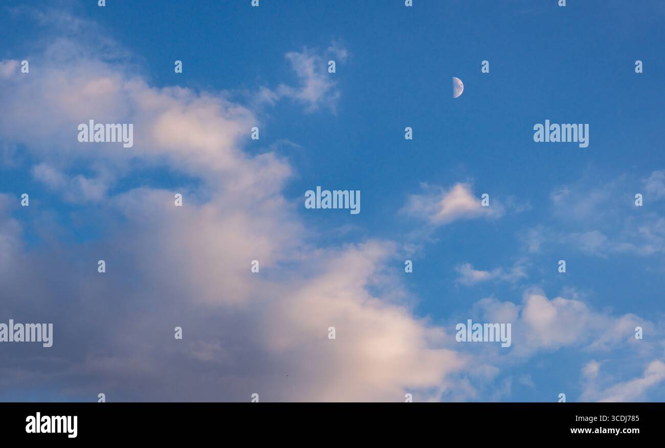A large moon is visible in the sky above a cloudy blue sky. The moon is the only object in the sky, and it is the main focus of the image. The sky is Stock Photo
