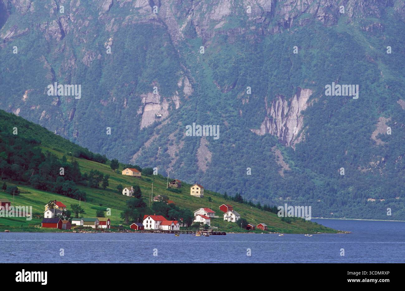 The village of Aldra, Helgeland. Buildings, homes, boat harbor and small farms. The huge rock, mainland in the background. Stock Photo