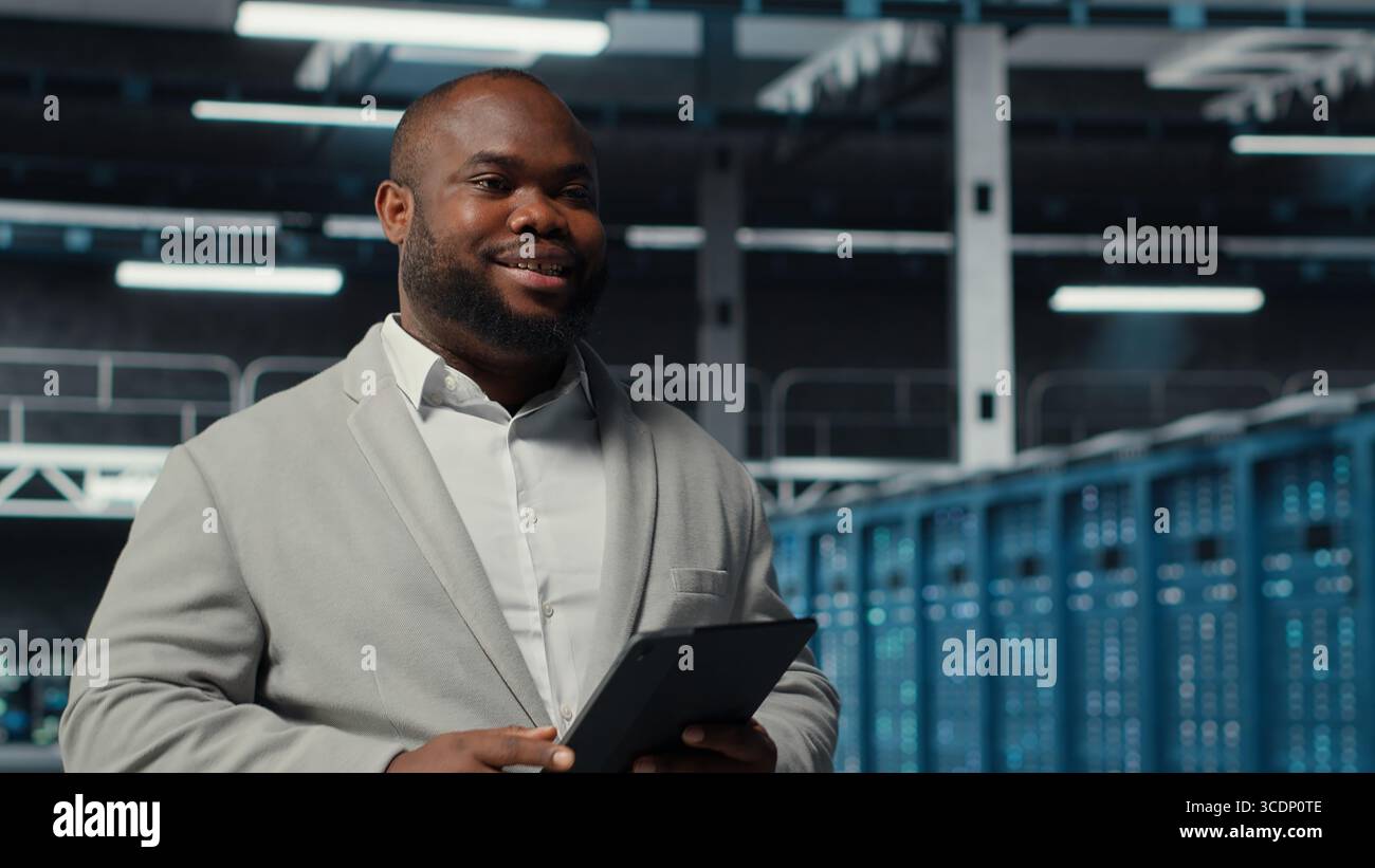 System administrator walking in server farm deploying infrastructure for efficient data analysis. Worker using device in dat a center in managing storage systems for datasets, camera B Stock Photo