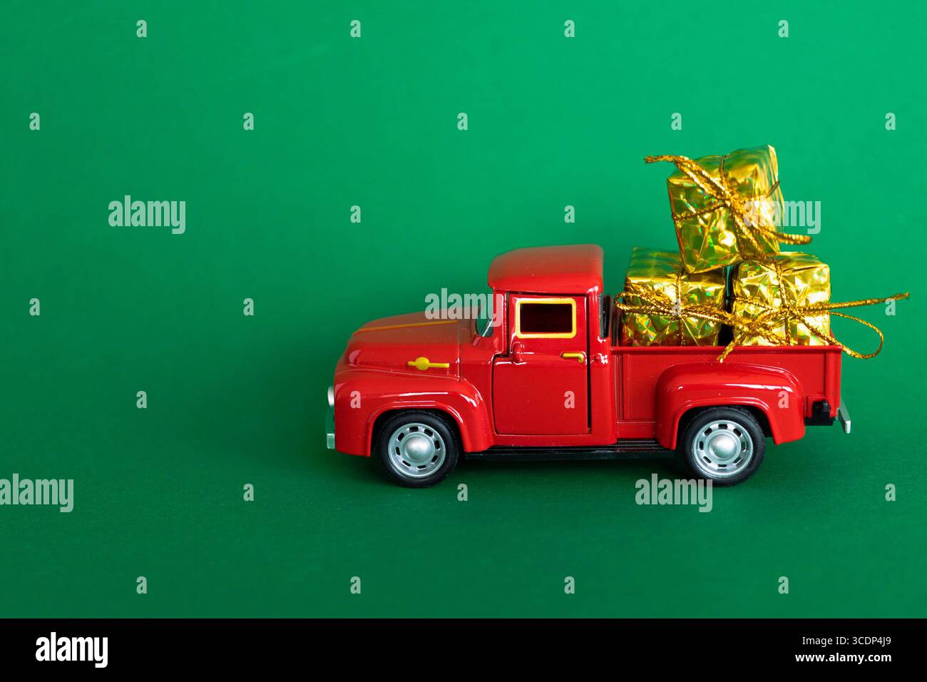 A red toy truck carrying gift boxes wrapped in gold paper, for Christmas, on a green background Stock Photo