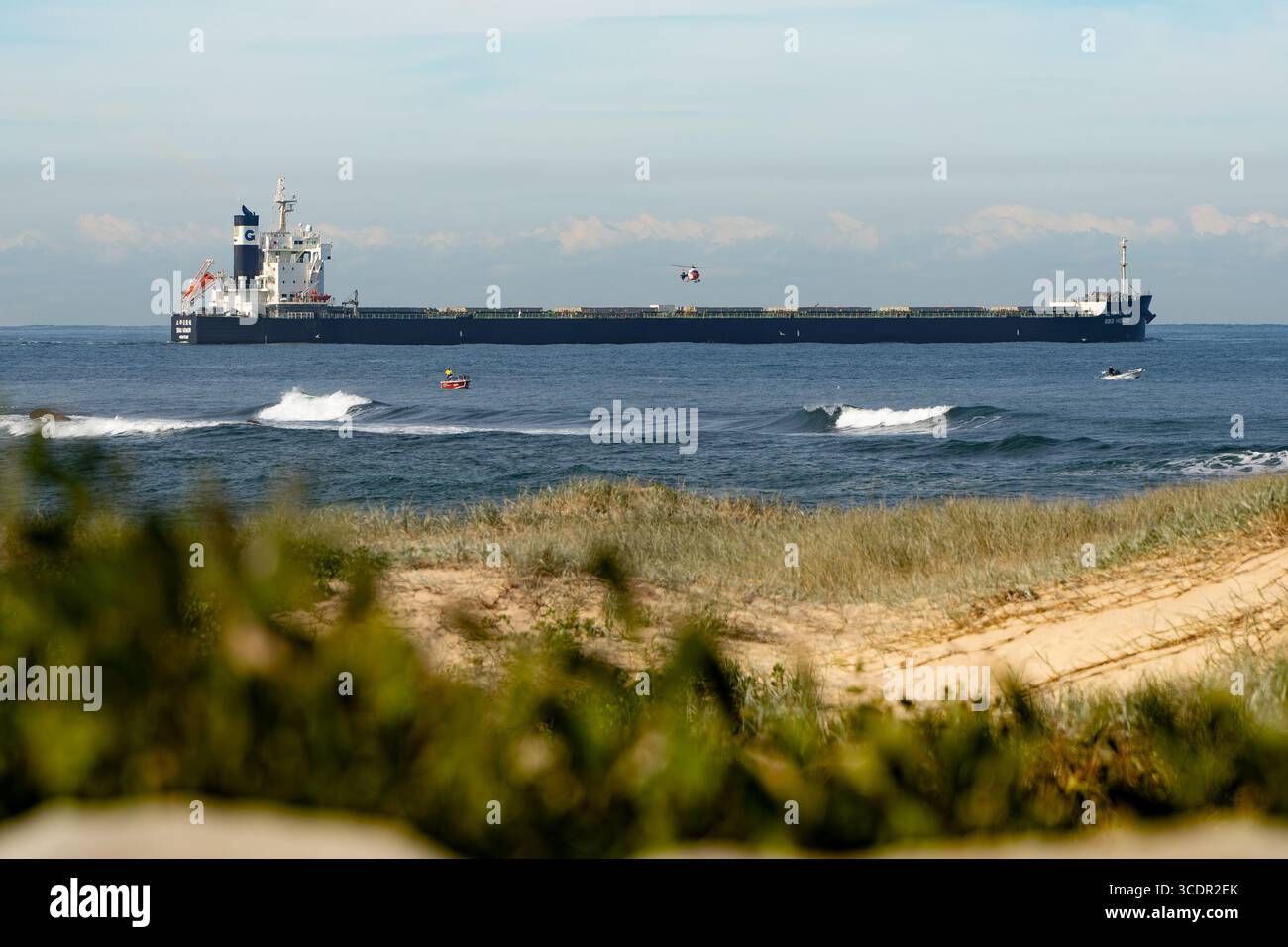 A helicopter comes into land on the deck of a cargo ship passing Nobbys Headland - Whibayganba - in Newcastle, New South Wales, Australia Stock Photo