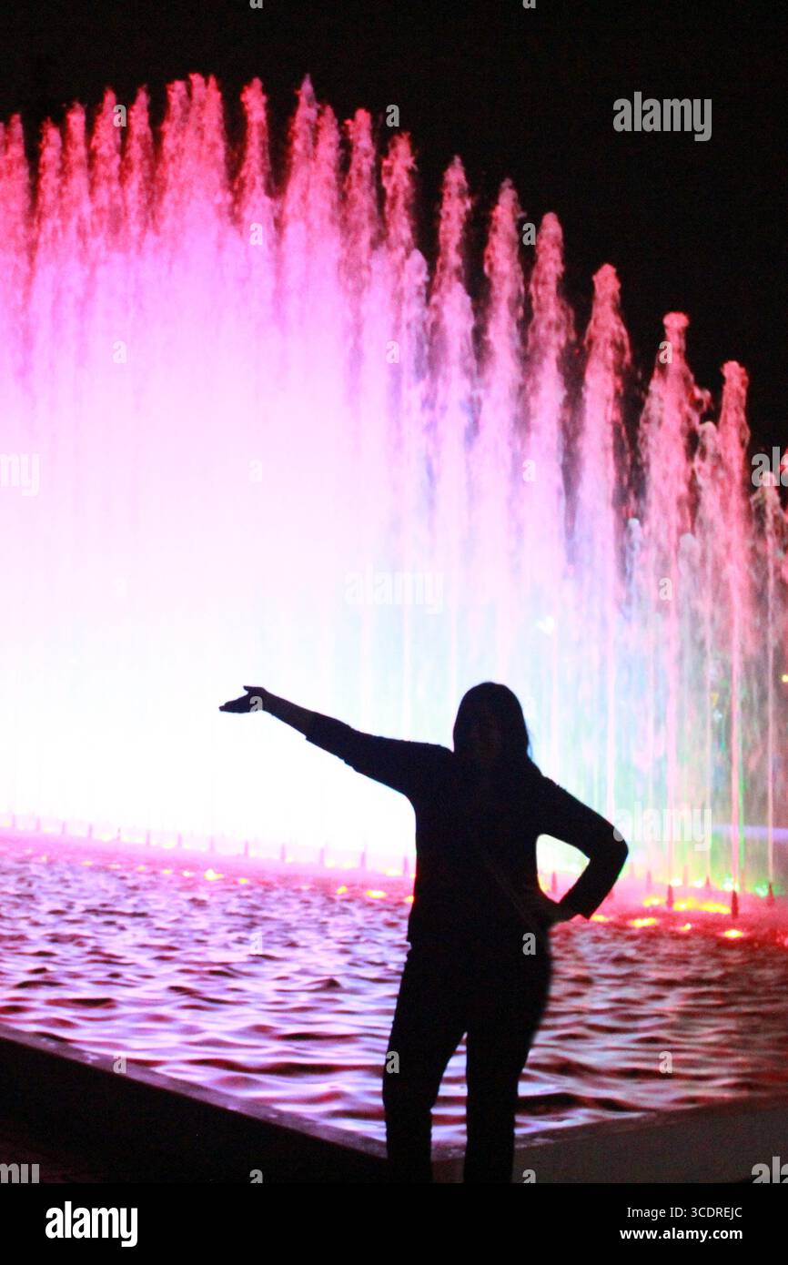 Silhouette of a woman in front of a lighted fountain during a walk at ...