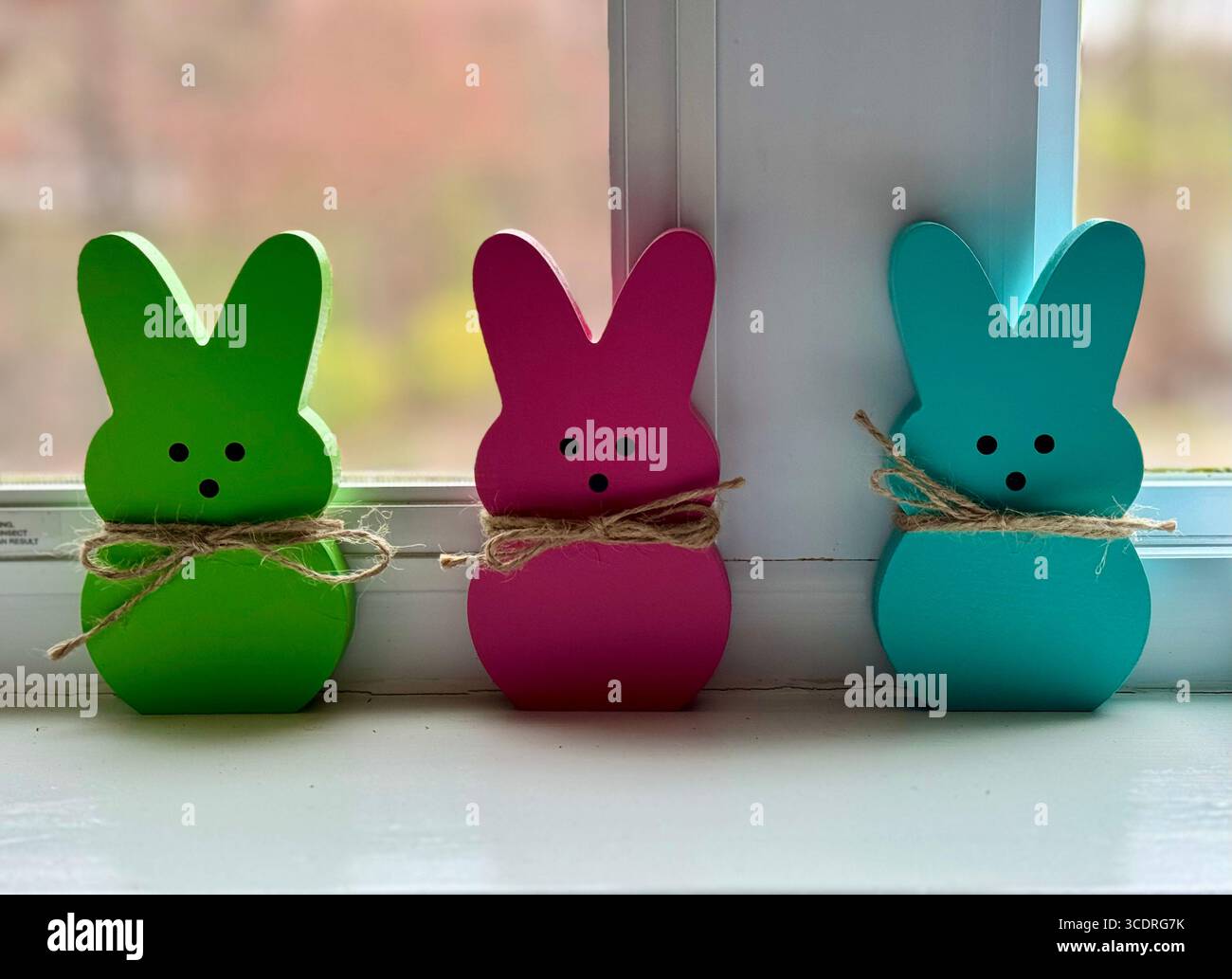 3 little wooden bunnies lined up against a window frame as part of Easter and springtime decoration. - Smartphone Captured Stock Image