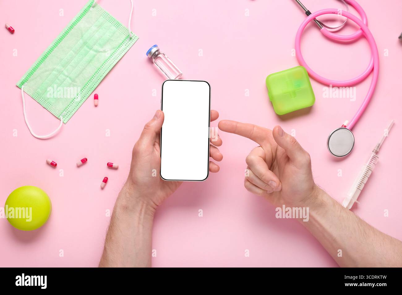 Male hands pointing at blank mobile phone and medical supplies on pink background Stock Photo