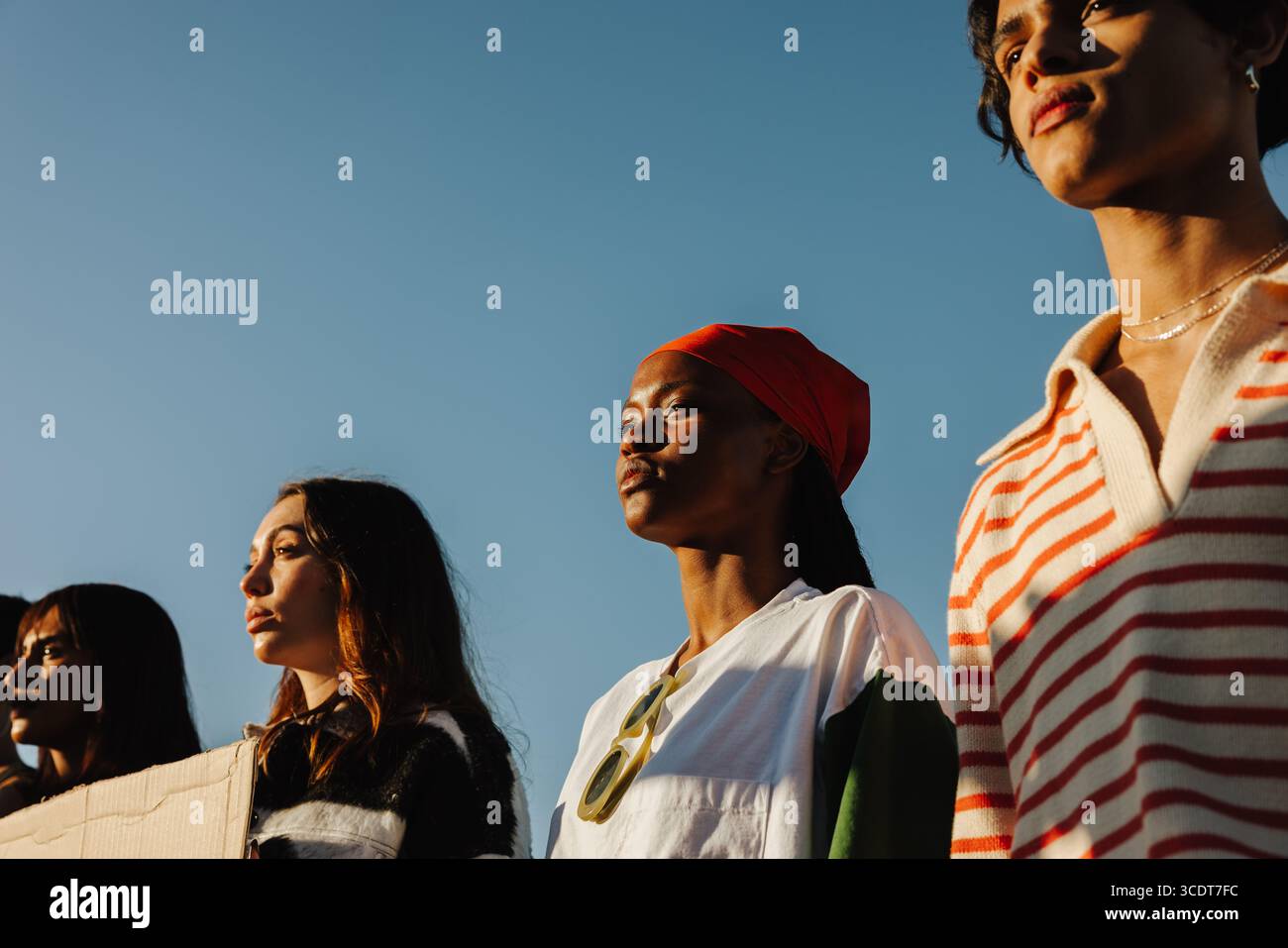 Diverse group of young people united at a peaceful outdoor protest, looking determinedly ahead. They stand under a clear sky, showcasing solidarity an Stock Photo