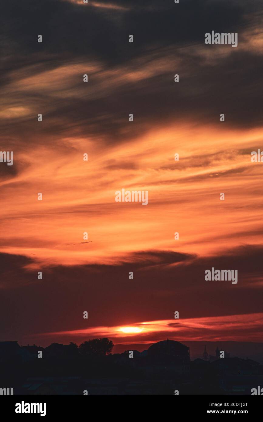 Abstract sky with soft orange-grey clouds and city skyline in silhouette at dusk. Stock Photo