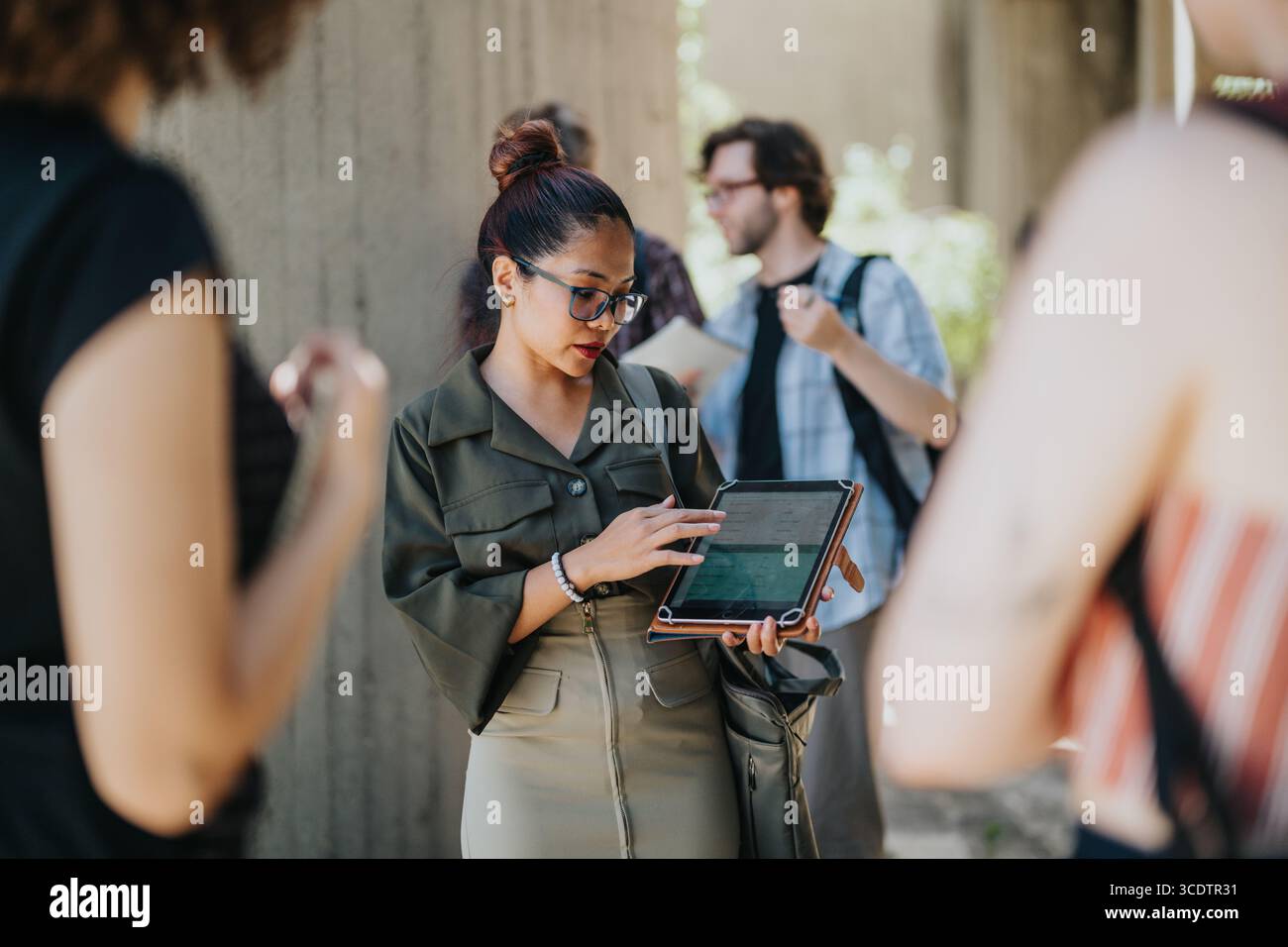 Female educator using a tablet while teaching students outdoors at a campus Stock Photo