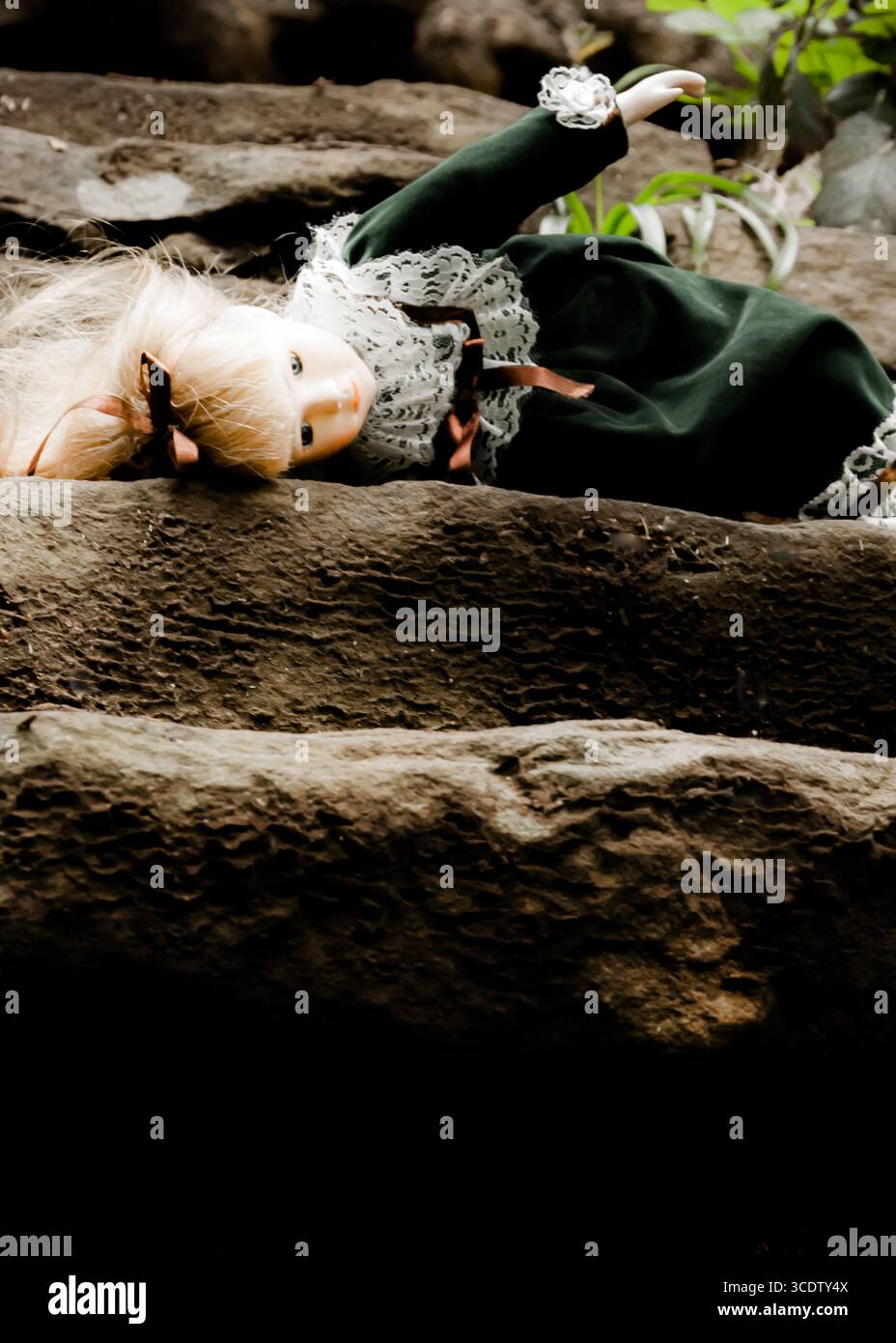 A doll with blonde hair and a green dress is lying on a stone surface. Stock Photo
