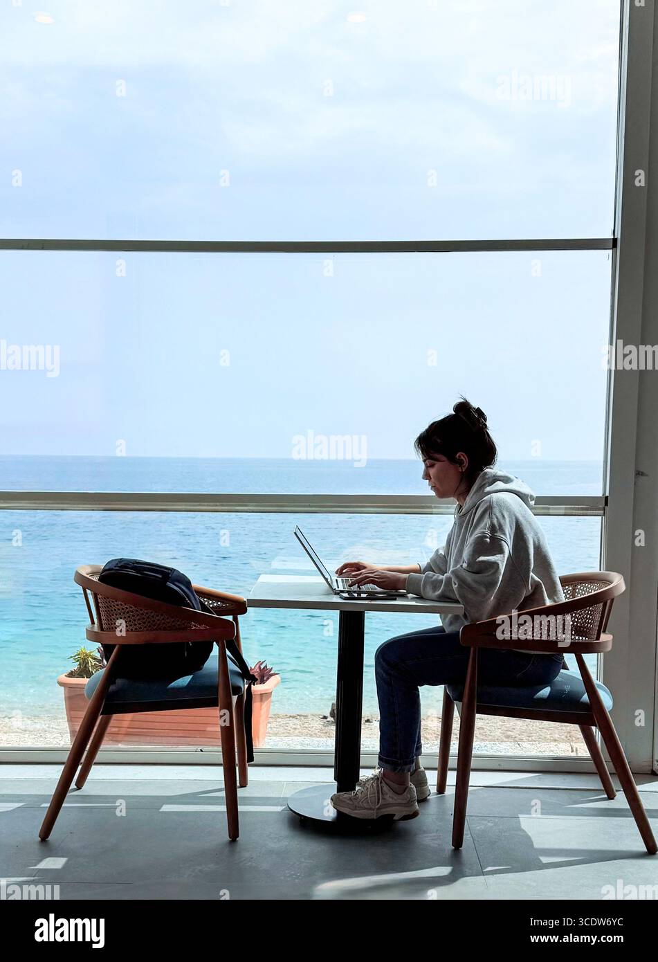 Antalya, Turkiye 03/17/2025: Co'ala coffee, dessert, fun. Co-working near the sea. Panoramic window, table, and laptop.Girl working online - Smartphone Captured Stock Image