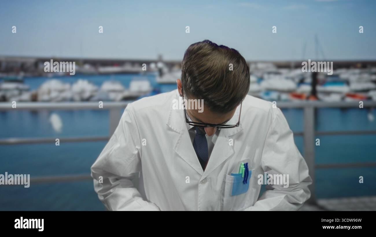 Young hispanic man scientist bends head down while adjusting white labcoat by port; scientific curiosity. Stock Photo