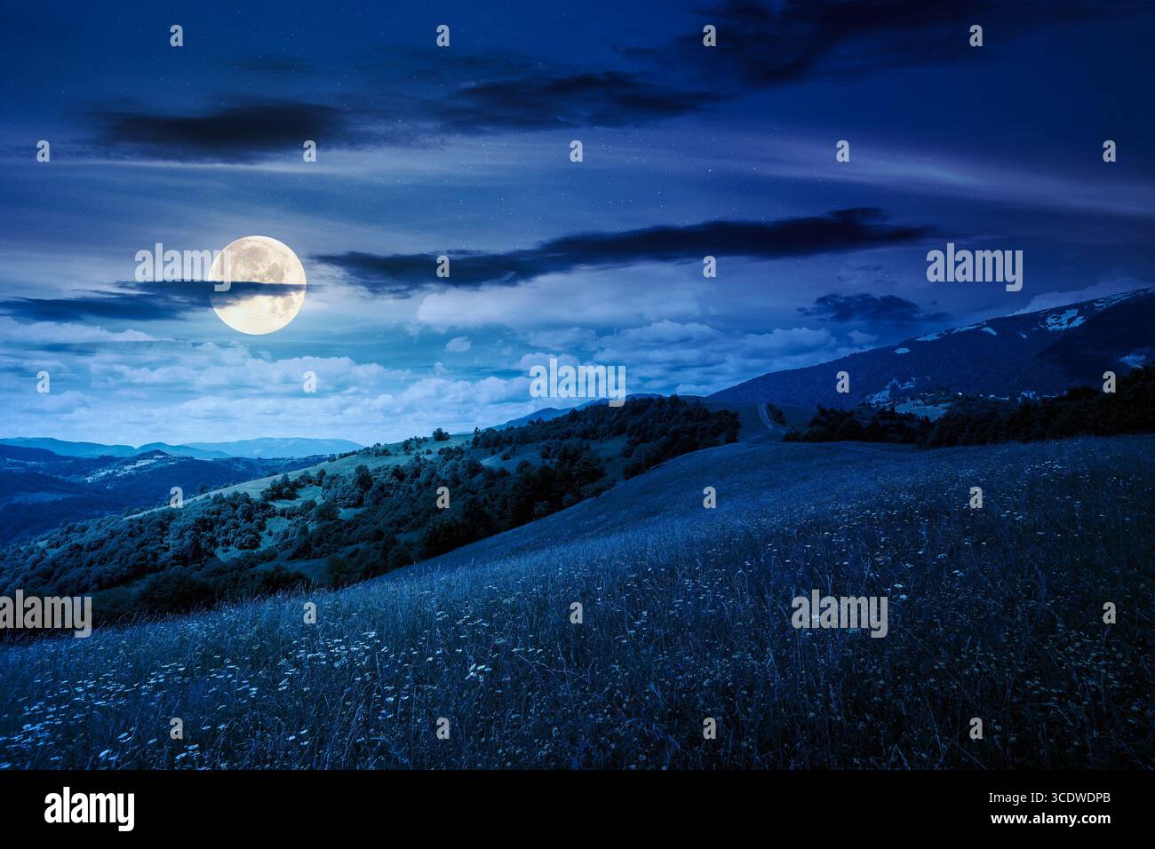 mountain landscape with wide meadow in summer at night. sky with dark clouds. grass on the pasture rolling through hills in countryside scenery to dis Stock Photo