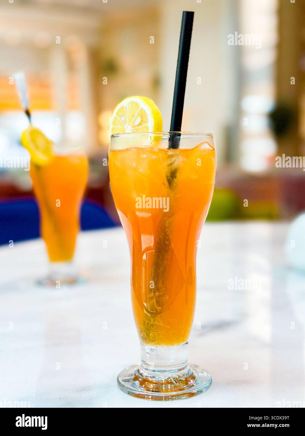 A tall glass of iced tea with lemon slices and a black straw on a marble table in a bright hotel bar setting in Dubai, UAE - Smartphone Captured Stock Image