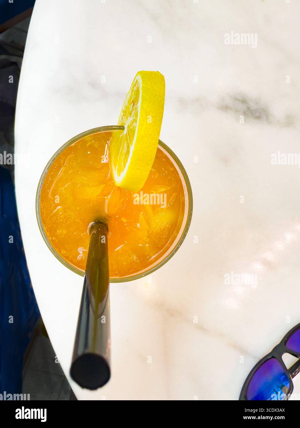 A tall glass of iced tea with lemon slices and a black straw on a marble table in a bright hotel bar setting in Dubai, UAE - Smartphone Captured Stock Image