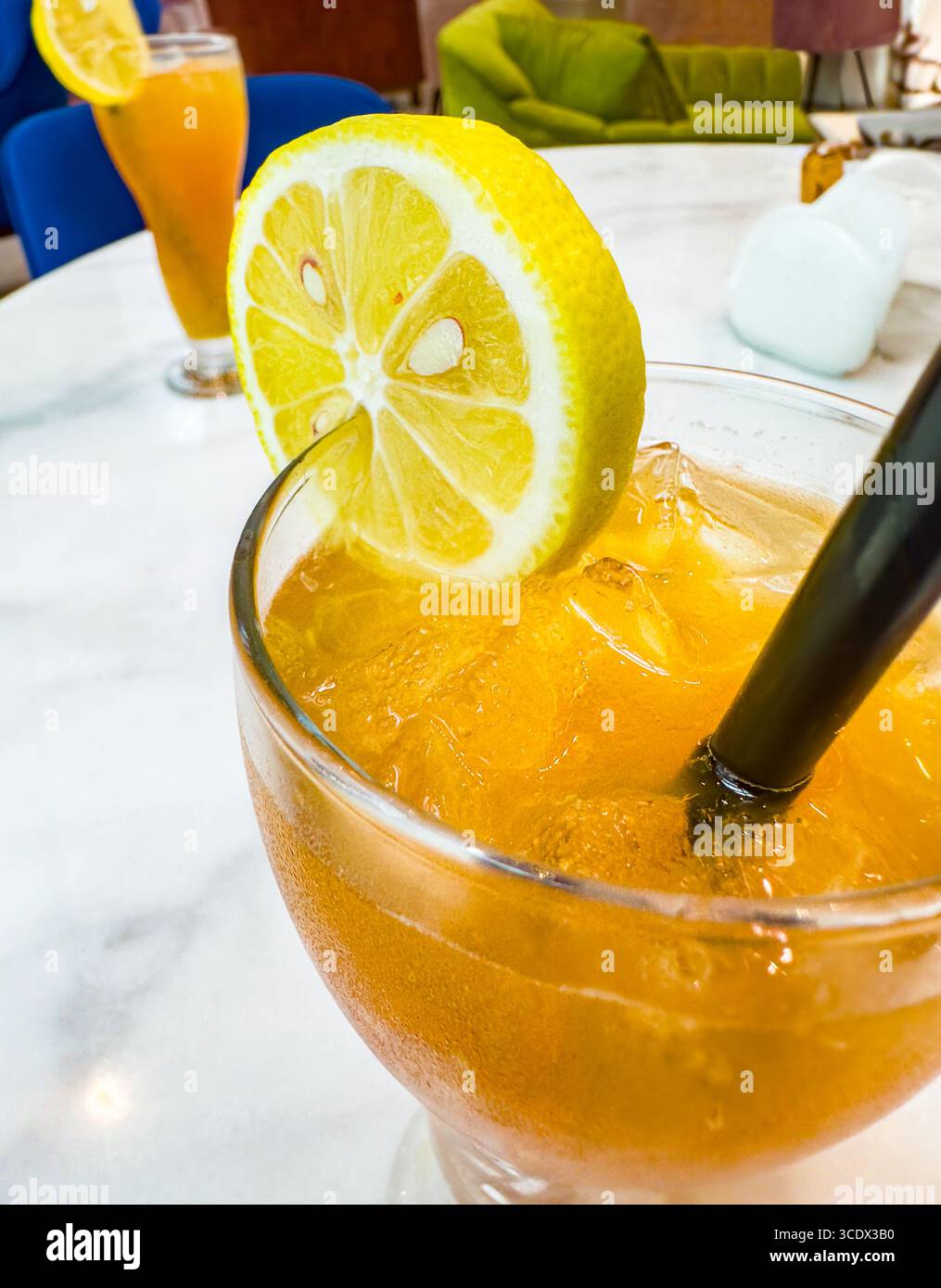 A tall glass of iced tea with lemon slices and a black straw on a marble table in a bright hotel bar setting in Dubai, UAE - Smartphone Captured Stock Image
