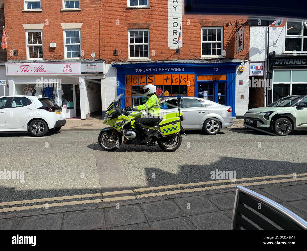 Policeman on a motorbike helmet stop arrest traffic police drive ride slow fast speed motorist road path outside station shops Market Harborough UK - Smartphone Captured Stock Image