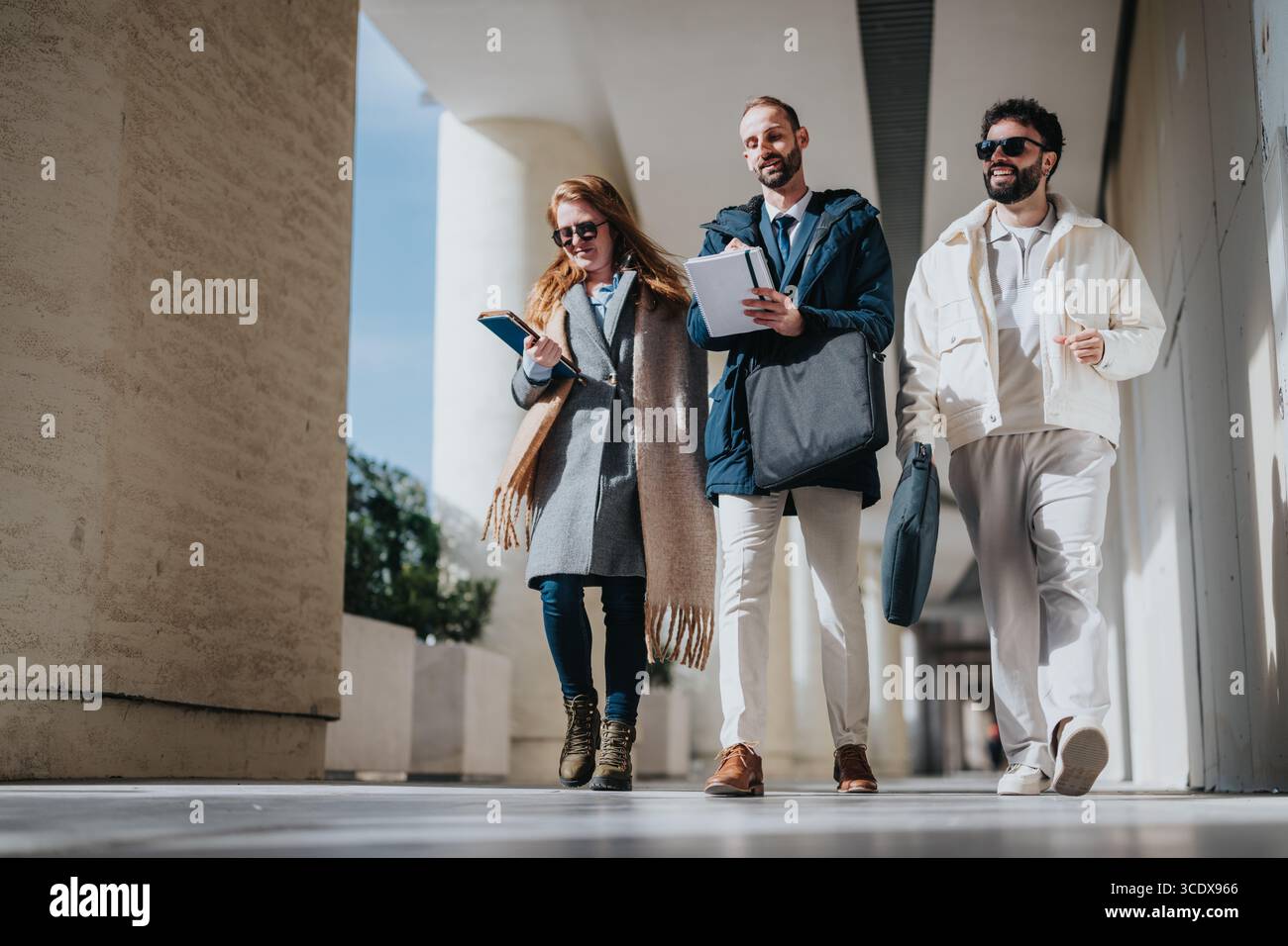 Three colleagues walking outdoors while discussing work and carrying documents Stock Photo