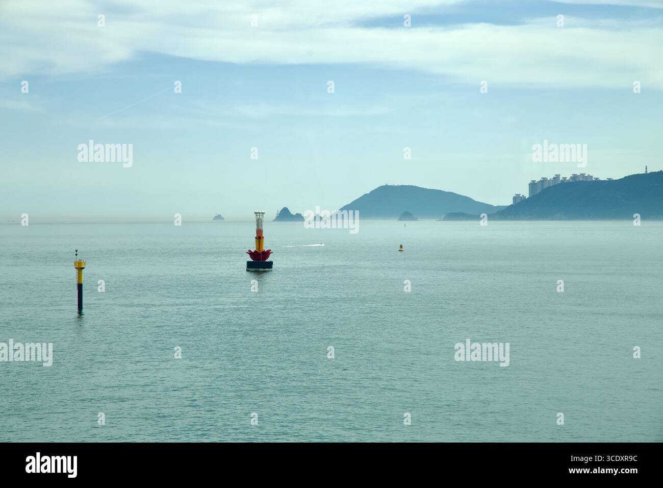 Navigation buoys stand in the East Sea off Busan with hazy offshore islets and wooded headlands in the distance on a calm summer day. Stock Photo