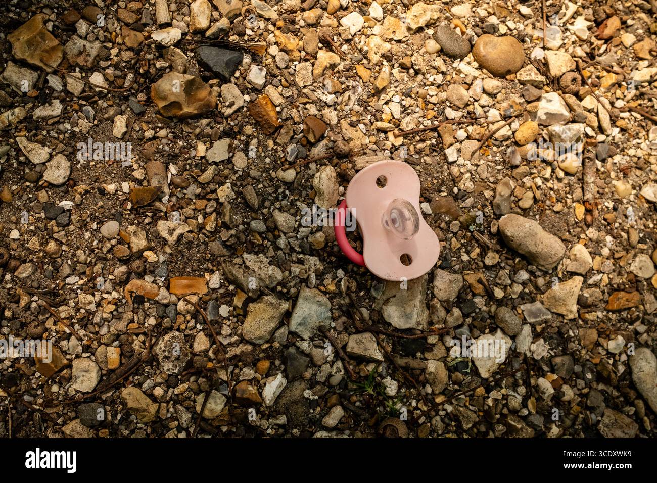 Childs pacifier or dummy, dropped, discarded and lost on a floor of shingle and stone Stock Photo