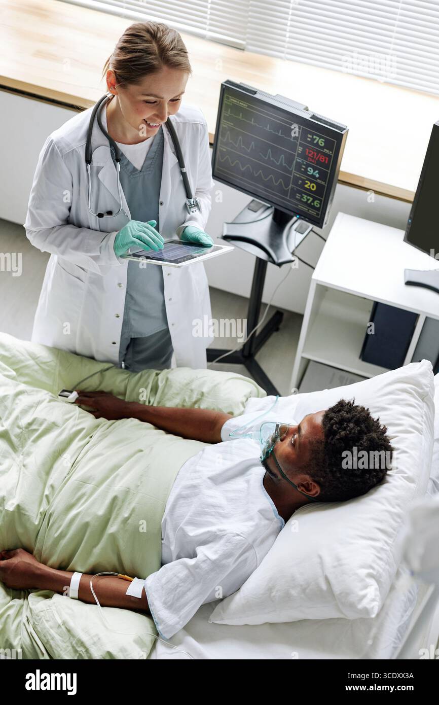 Vertical high angle view of cheerful young adult doctor greeting young Black man after waking up from coma Stock Photo