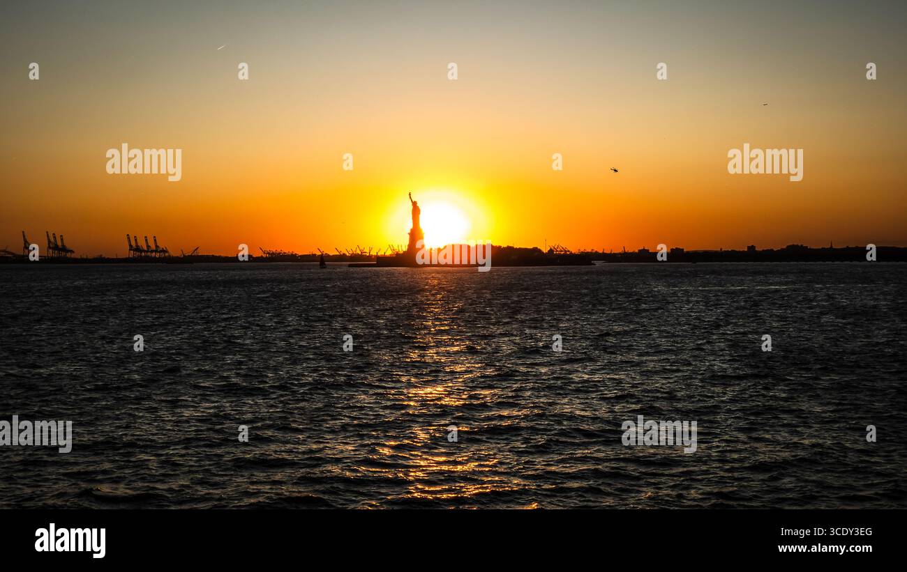 The sun sets behind The Statue of Liberty as seen from the Staten Island Ferry - Smartphone Captured Stock Image