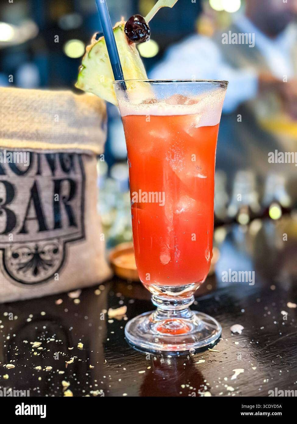 A refreshing singapore sling cocktail garnished with a pineapple slice and cherry, at the elegant Long bar at Raffles hotel singapore scattered nuts - Smartphone Captured Stock Image