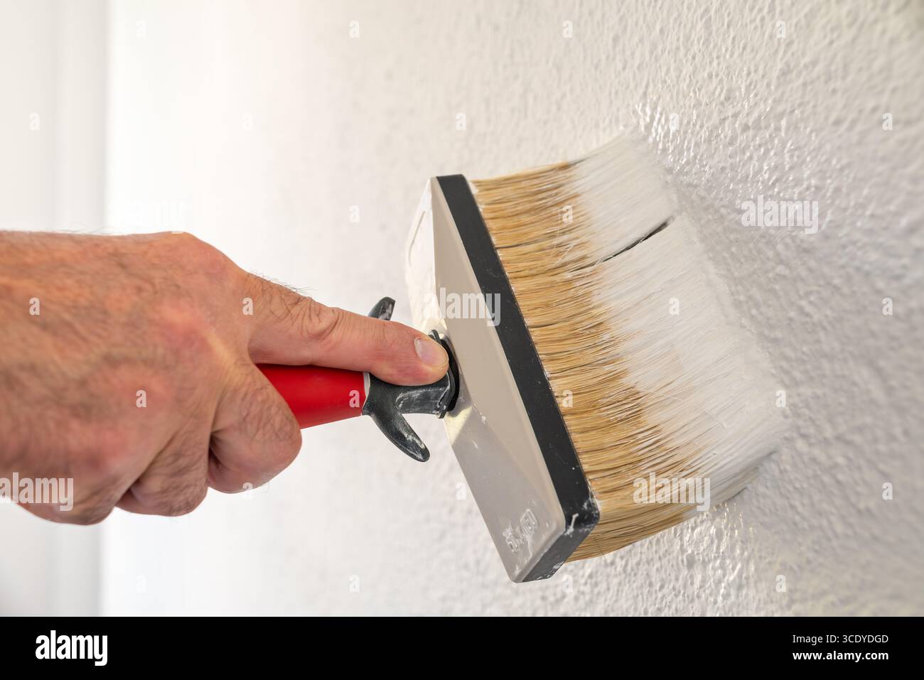Close-up of a hand. A painter paints a masonry wall with white paint using using the paintbrush. Construction industry. Stock Photo