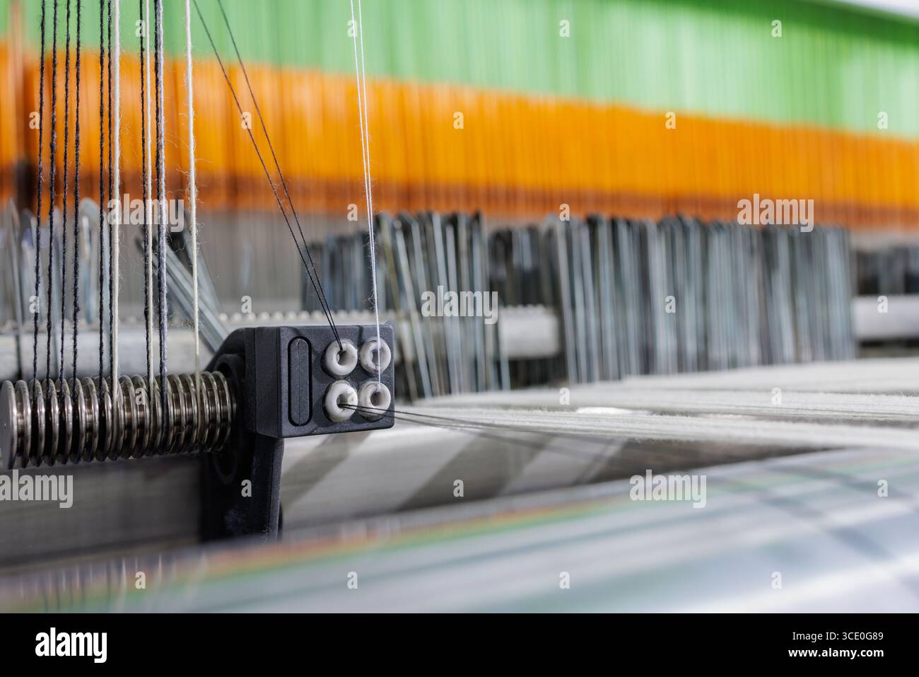 Macro detail of wool warp passing a tensioner on a modern weaving machine, showing precision textile manufacturing for industry and automation. Stock Photo