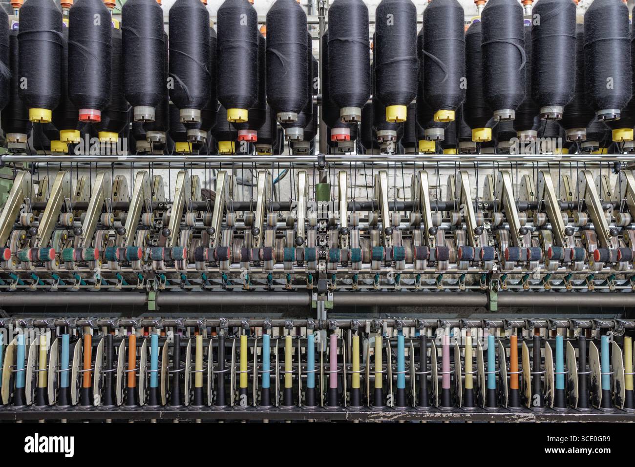 Front view of an automated spinning frame with black yarn cones and ...