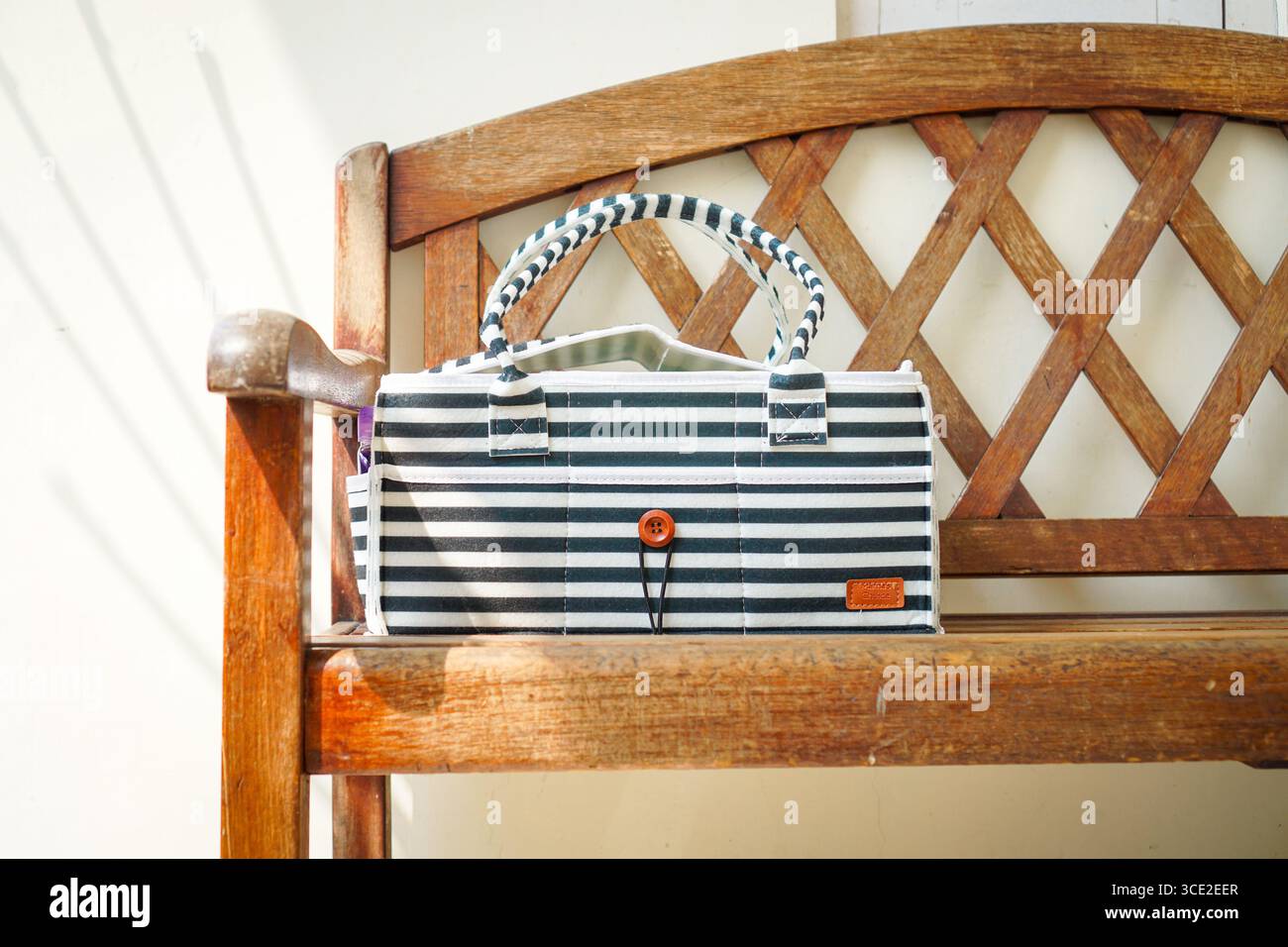 Striped fabric handbag with button detail on a wooden bench in natural light, minimalist lifestyle and eco friendly fashion accessory. Stock Photo