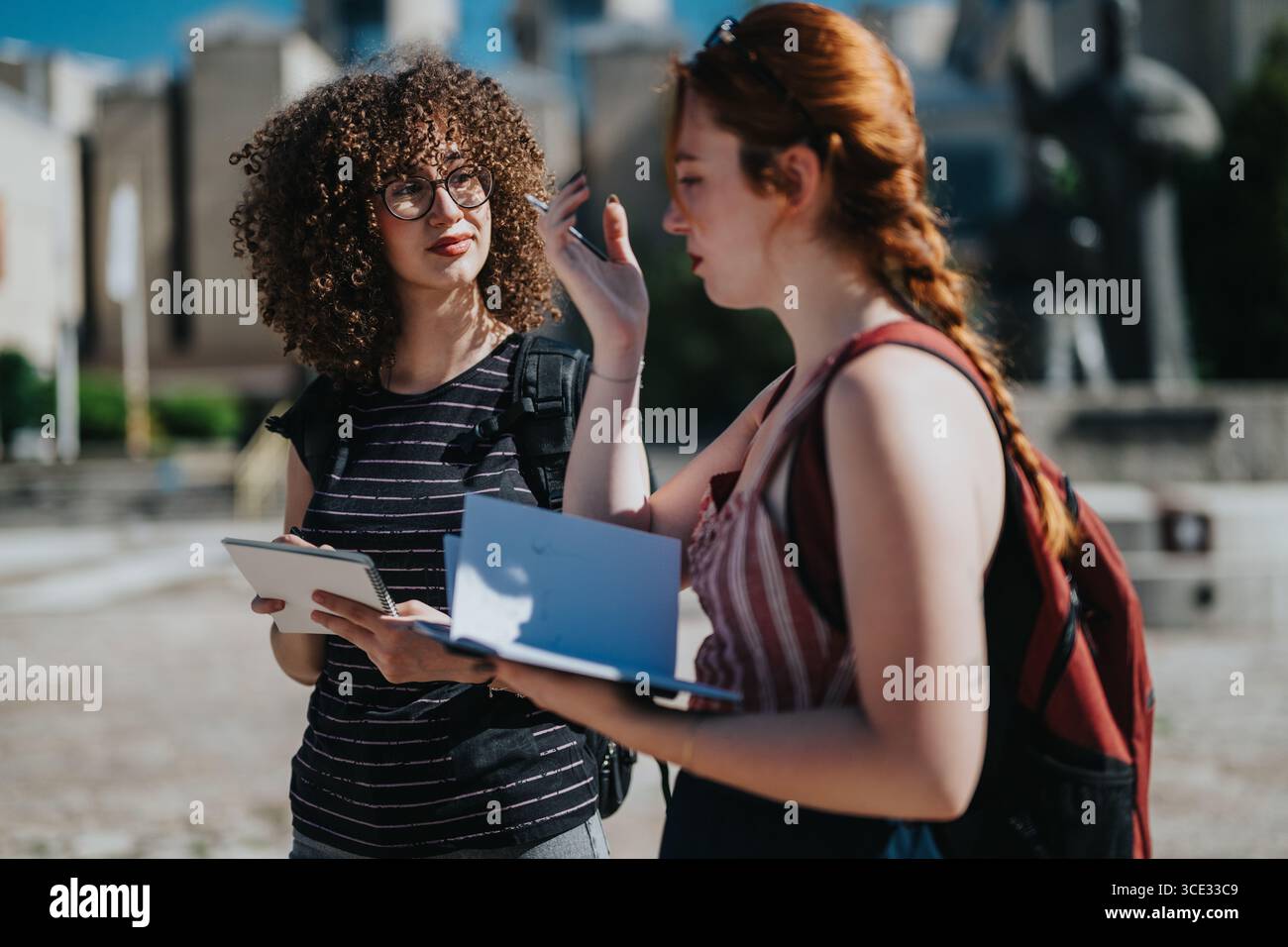 Two students discussing notes in a sunny outdoor courtyard area Stock Photo