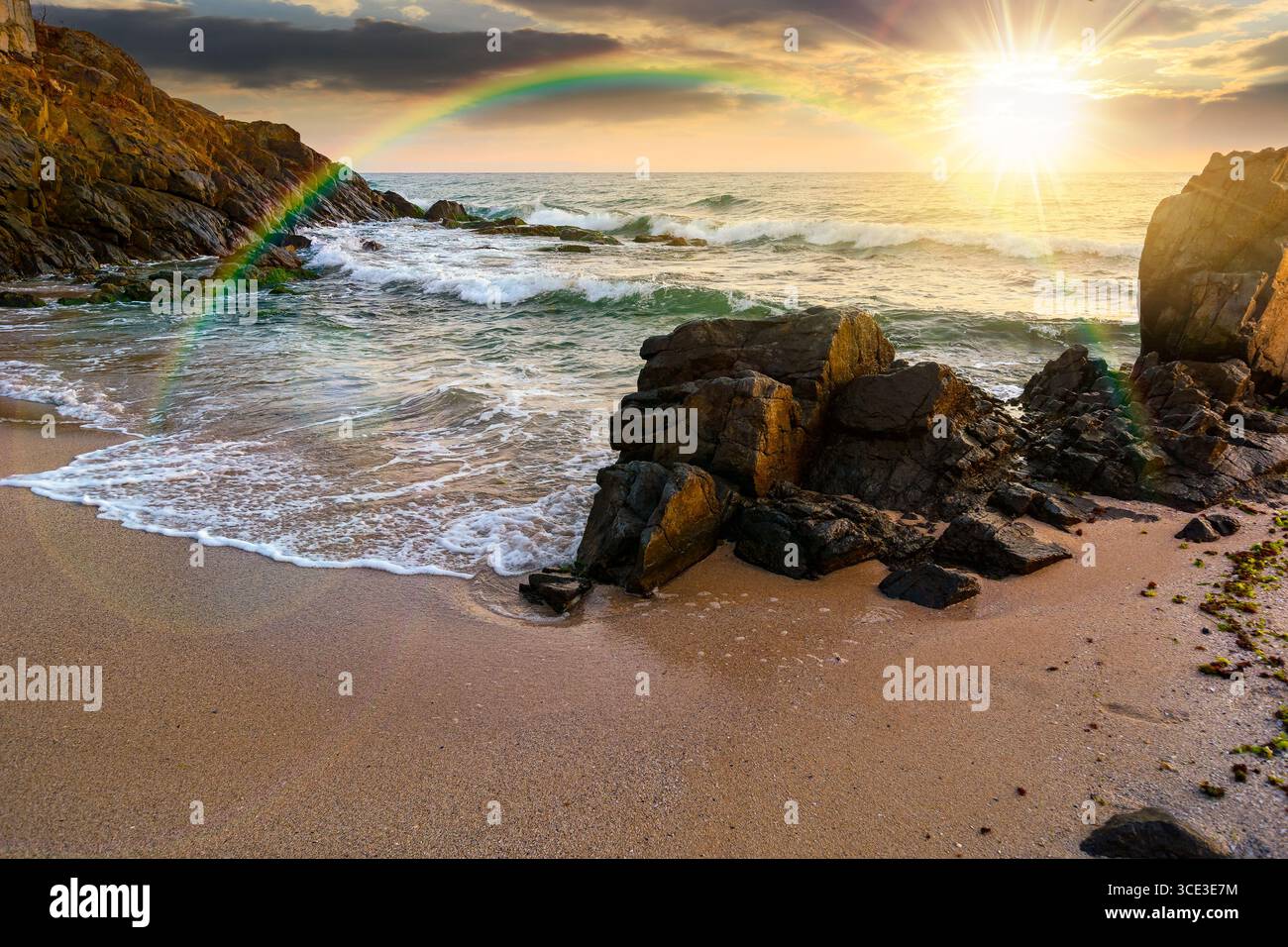 landscape by the sea at sunset in summer. beautiful beach with rocks washed by calm waves in evening light. view to horizon under rainbow and  blue sk Stock Photo
