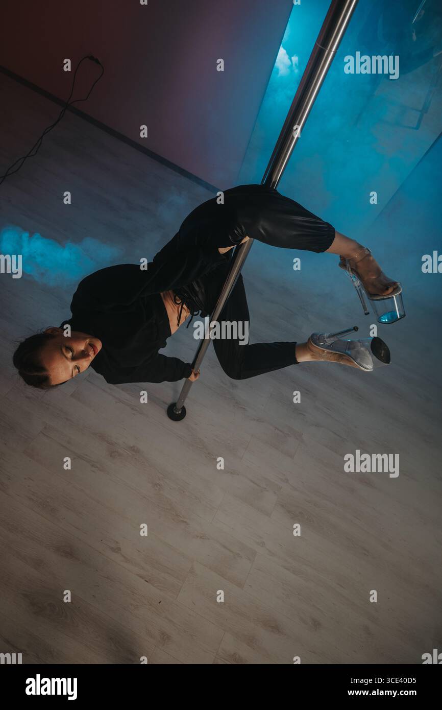 Woman performing artistic pole dance in a dynamic studio setting Stock Photo