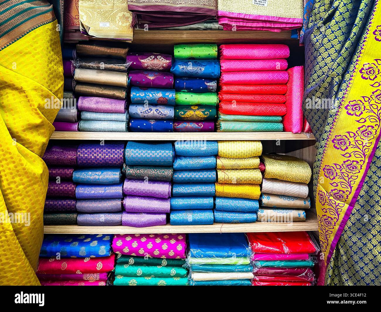 Colorful display of neatly stacked silk and fabric rolls in vibrant hues on wooden shelves in a textile shop interior malaysia - Smartphone Captured Stock Image
