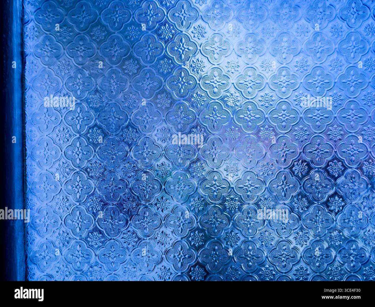 Close-up of a decorative frosted glass window with intricate floral patterns and a blue tint.  malaysia - Smartphone Captured Stock Image