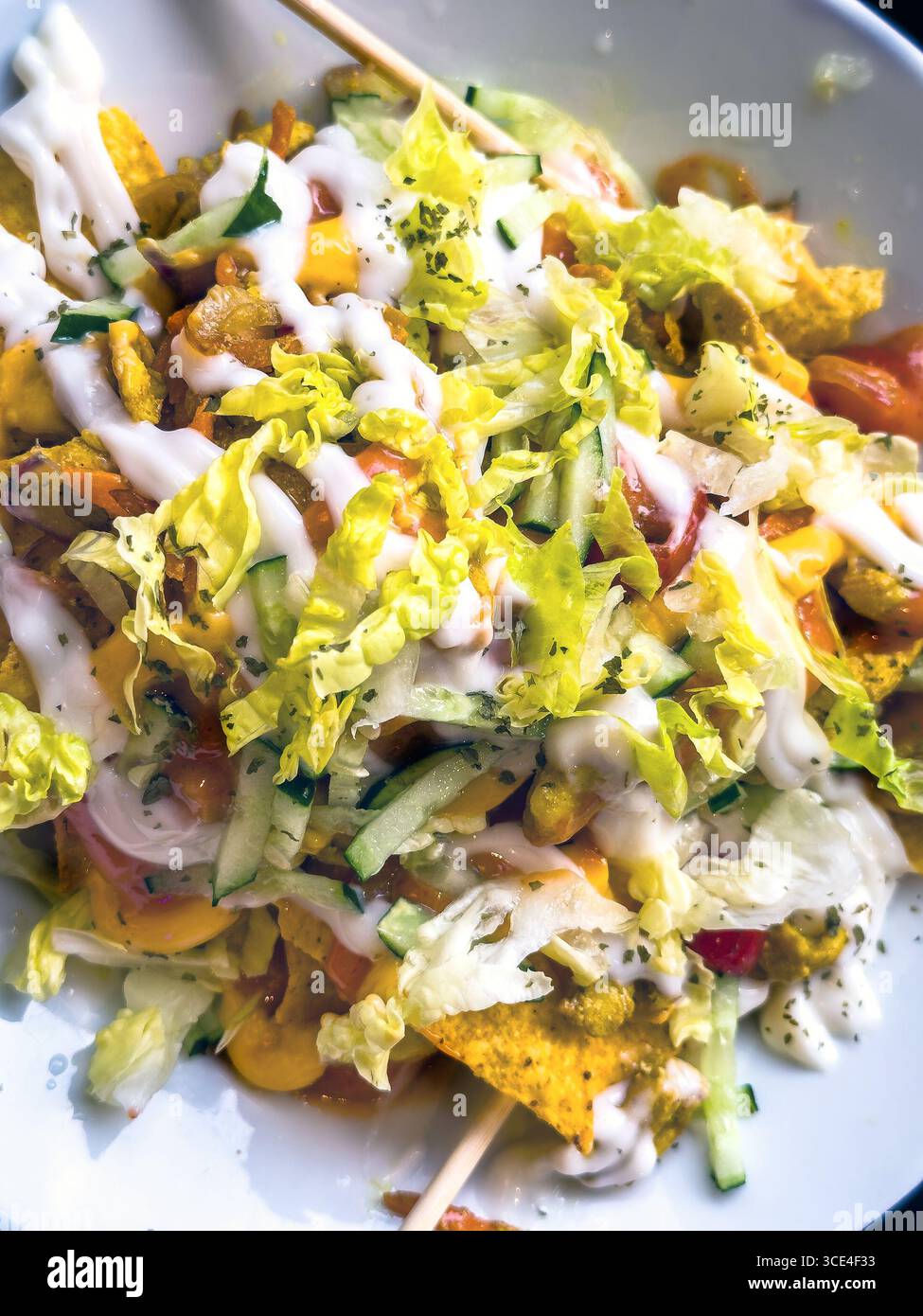 detail close up of Colourful vegetarian taco salad with nachos, fresh lettuce, tomatoes, cucumbers, and creamy dressing in a white bowl. malaysia - Smartphone Captured Stock Image