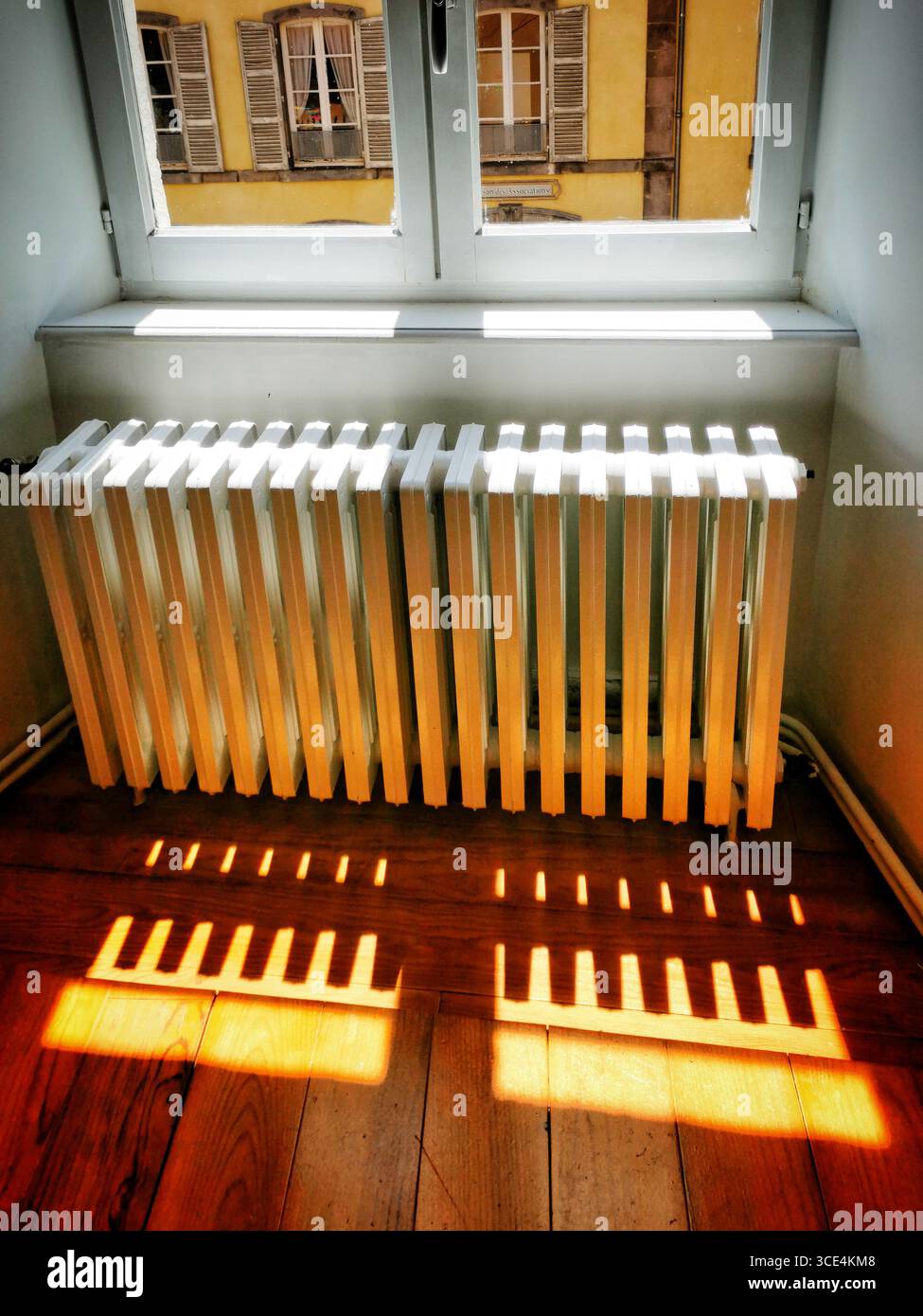 Sunlight streams through a window, creating patterned shadows on a white radiator. The wooden floor adds warmth, highlighting the inviting atmosphere - Smartphone Captured Stock Image