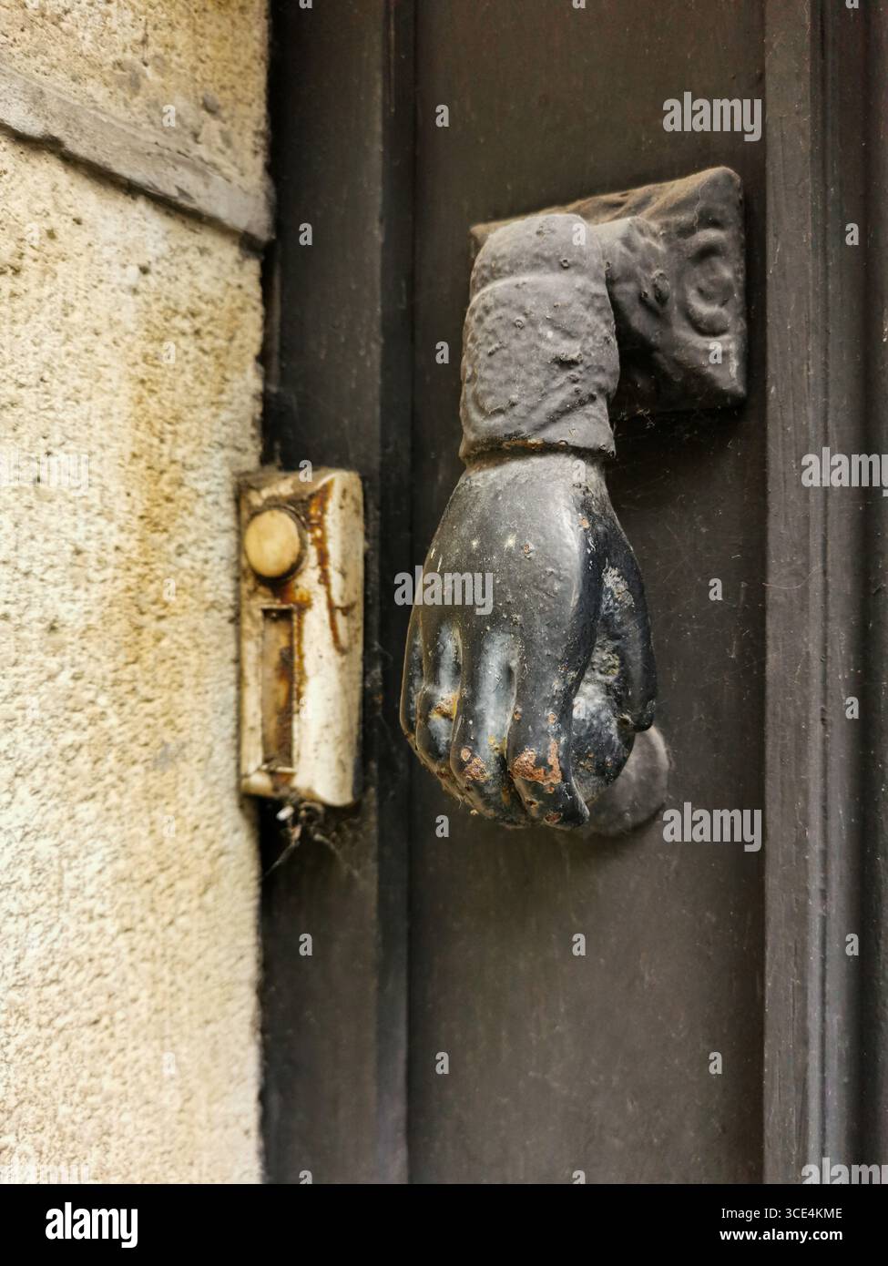 A striking hand-shaped door knocker is mounted on a weathered entrance. Beside it, an old doorbell adds charm, France - Smartphone Captured Stock Image