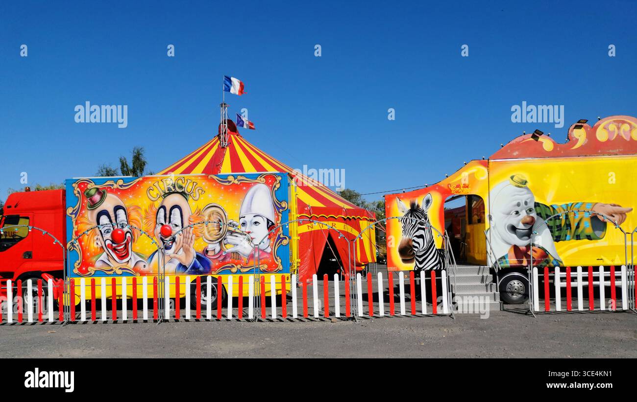 Vibrant circus tent adorned with bright colors and clown imagery, alongside distinctive vehicles. France - Smartphone Captured Stock Image