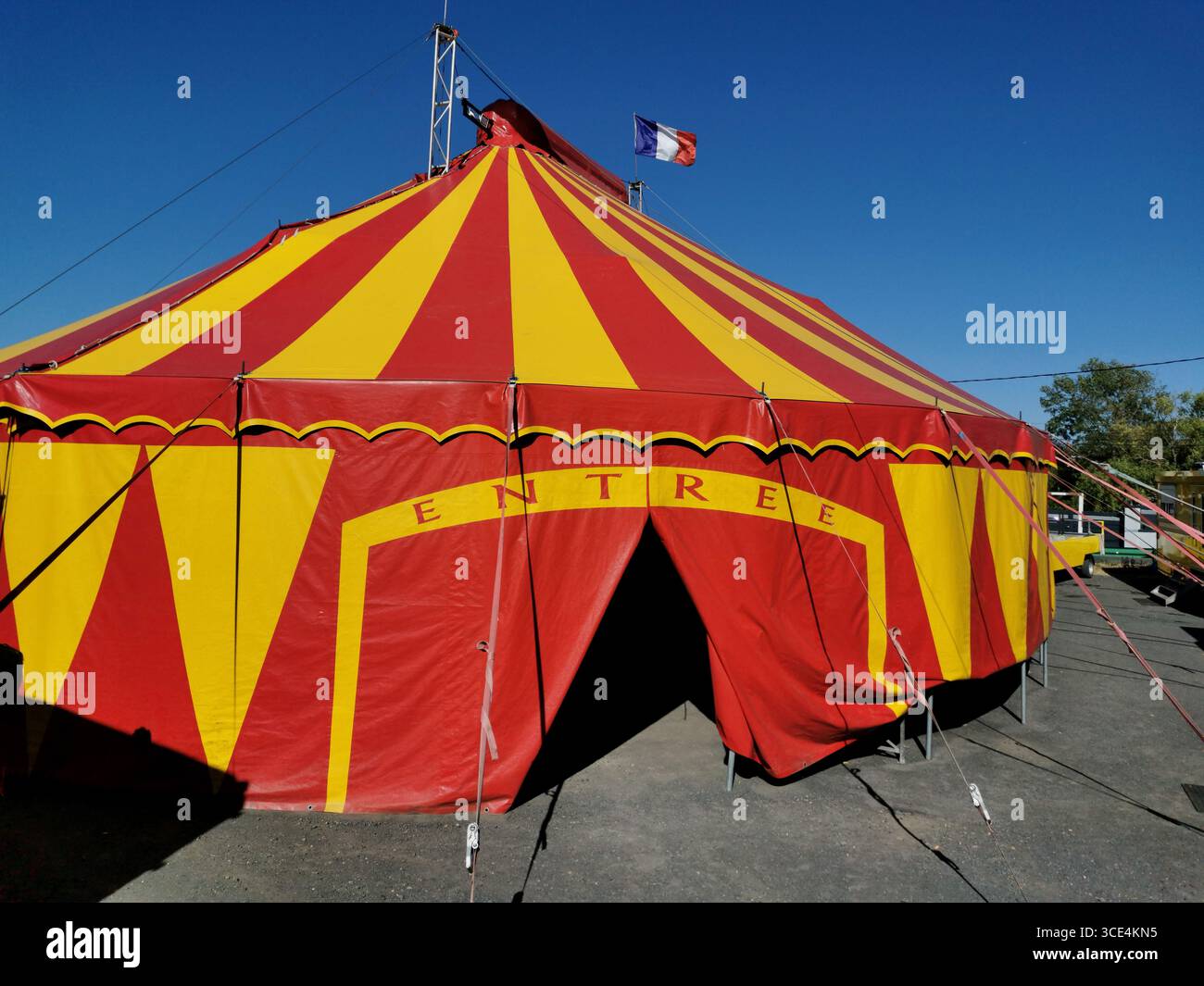 A large red and yellow circus tent welcomes visitors with a prominent entrance. Flags representing France wave in the breeze - Smartphone Captured Stock Image
