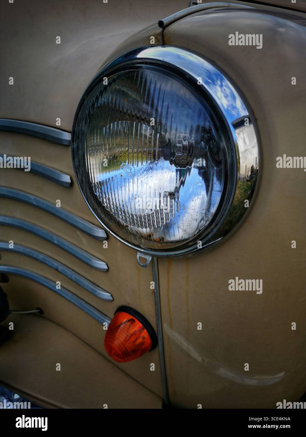 An old vintage car headlight glistens in the sunlight, capturing reflections of the surrounding nature. Rust and wear visible hint at its age - Smartphone Captured Stock Image