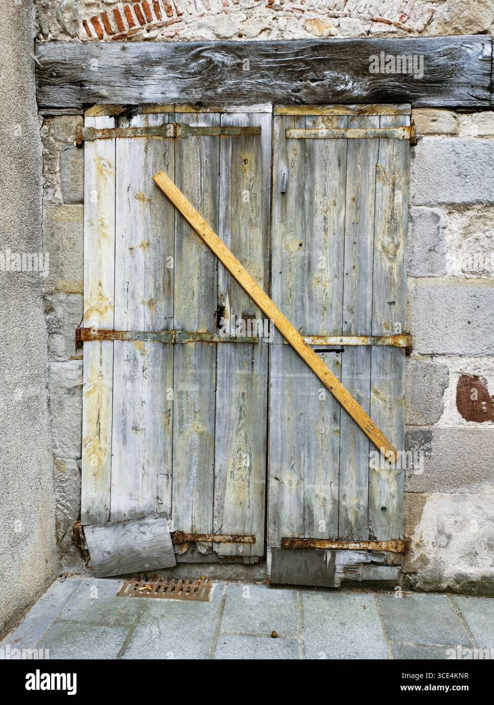 Old wooden door show signs of wear and decay, bolted with a plank. The stone wall surrounding them adds to the rustic charm. France - Smartphone Captured Stock Image