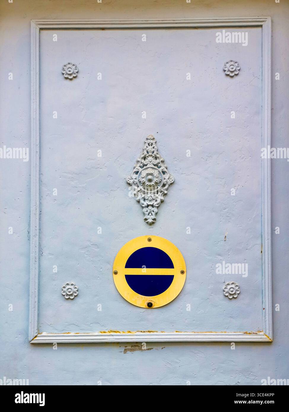 An ornate door showcases a no parking sign emblem on a pastel-colored wall in a serene neighborhood, France Stock Photo