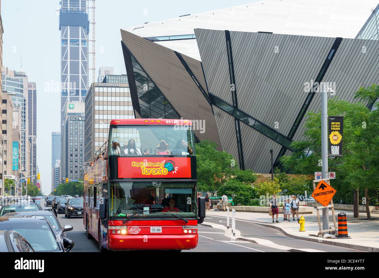 A red double-decker sightseeing bus drives past the angular facade of the Royal Ontario Museum under a clear sky. Stock Photo