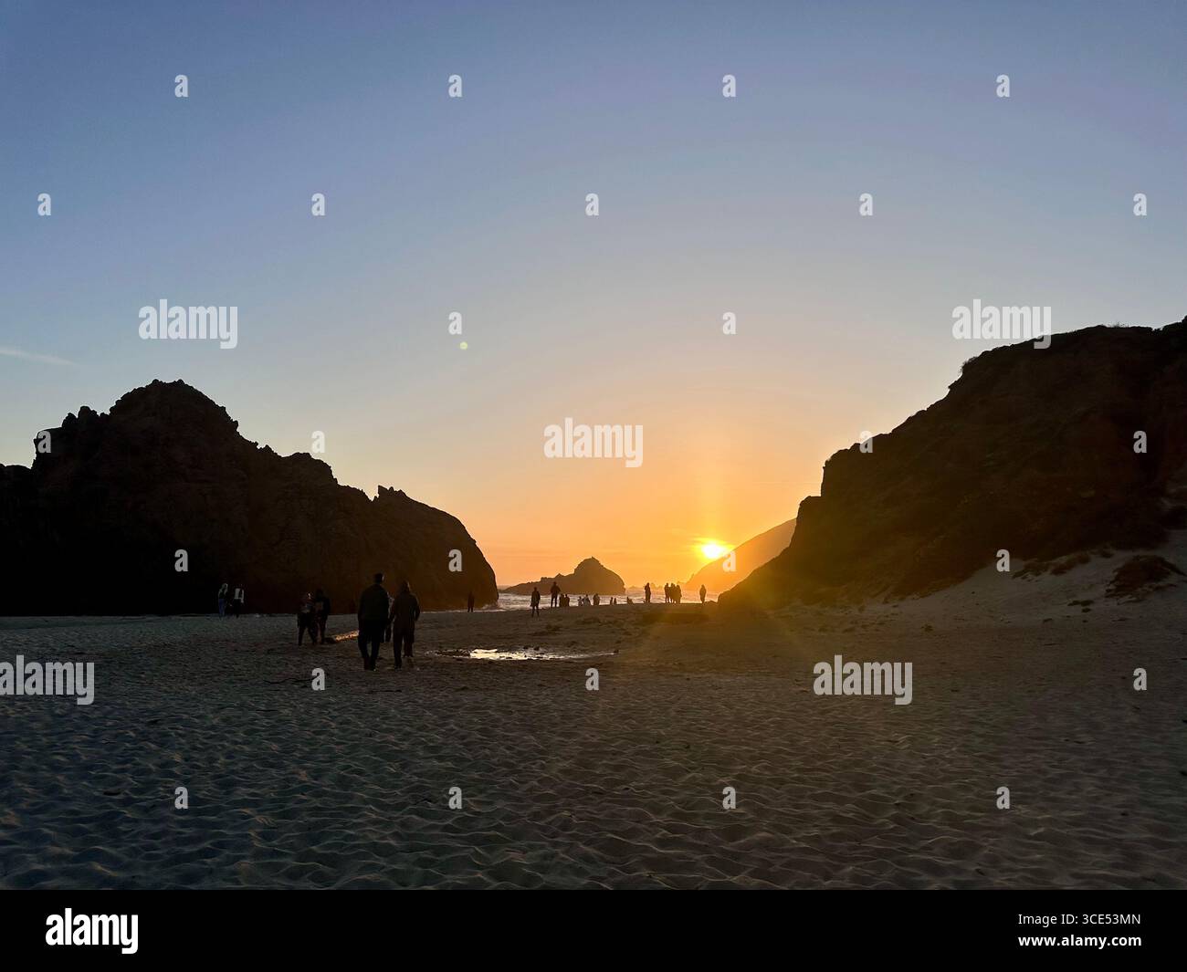 Golden sunset over the Pacific Ocean with waves washing onto the sandy beach and rugged cliffs in the background. - Smartphone Captured Stock Image