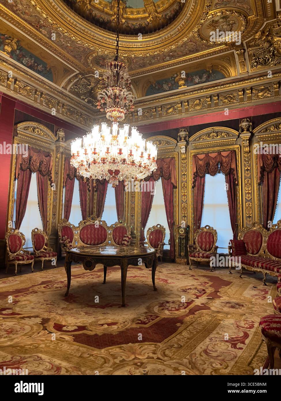 Opulent Dolmabahçe Palace room in Istanbul, featuring crystal chandelier, red velvet chairs, gold decorations, and rich carpets. - Smartphone Captured Stock Image
