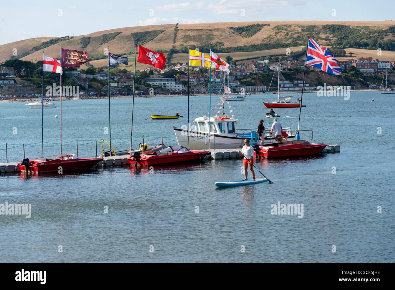 Swanage Dorset England UK. 02.08.2025. Motorboat hire business on Swange Bay with a paddle boarder and scenic hills. Stock Photo