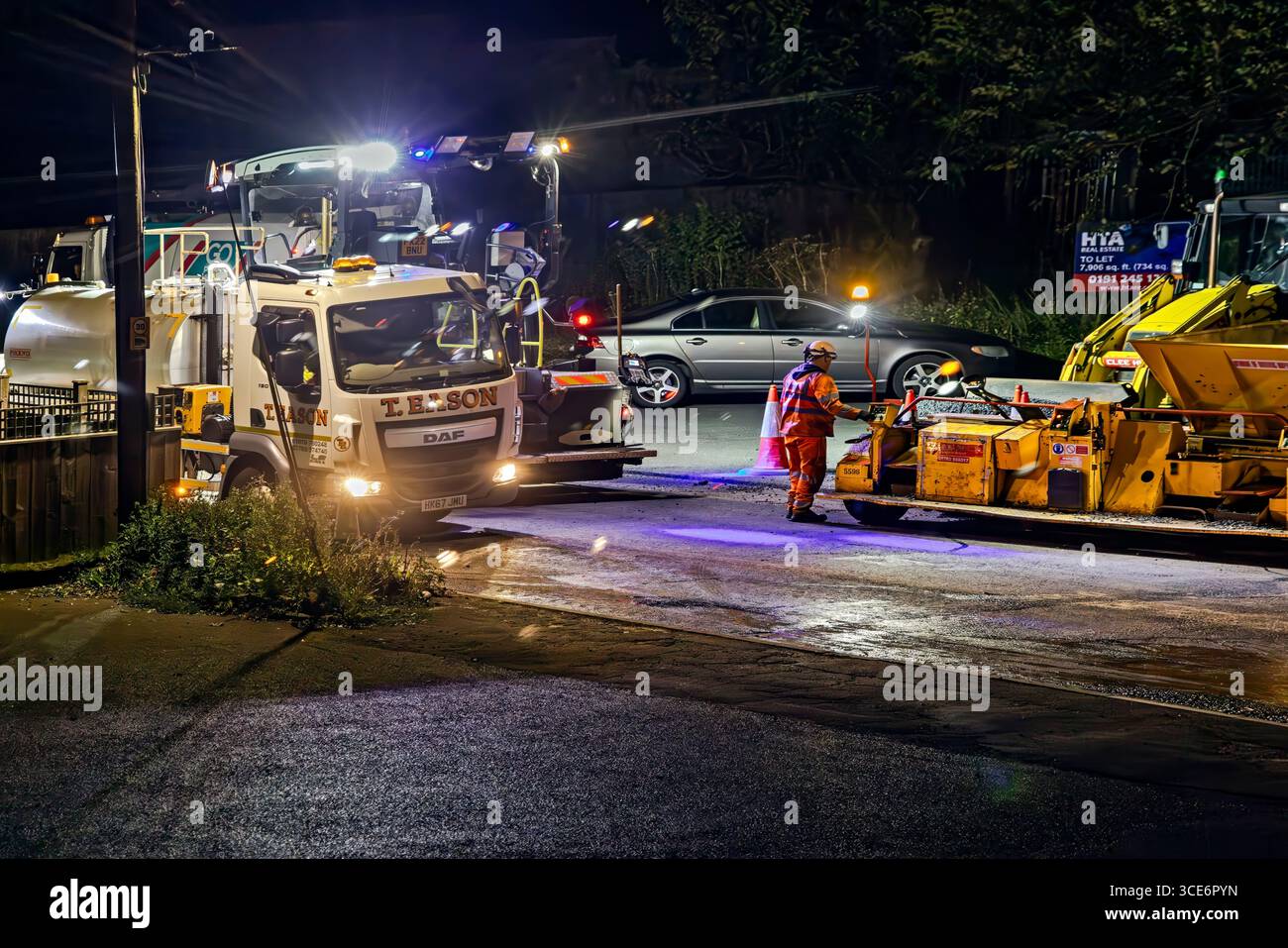 Road construction workers, machinery and equipment, resurfacing carriageway at night, Stokesley, North Yorkshire, England, UK Stock Photo