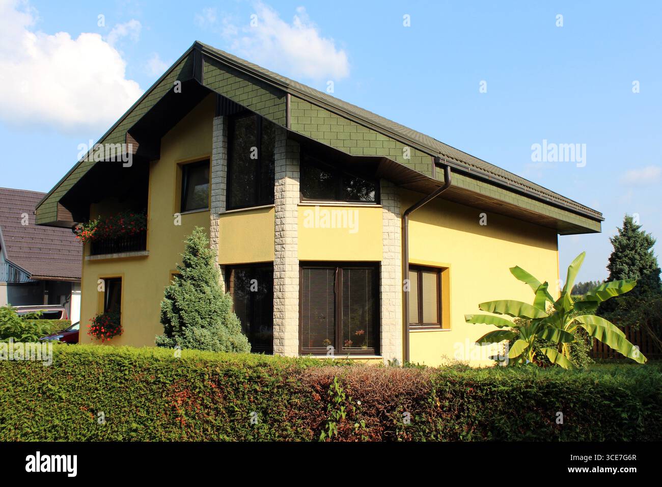 Stylish yellow home features green shingle roof, stone pillars, large ...