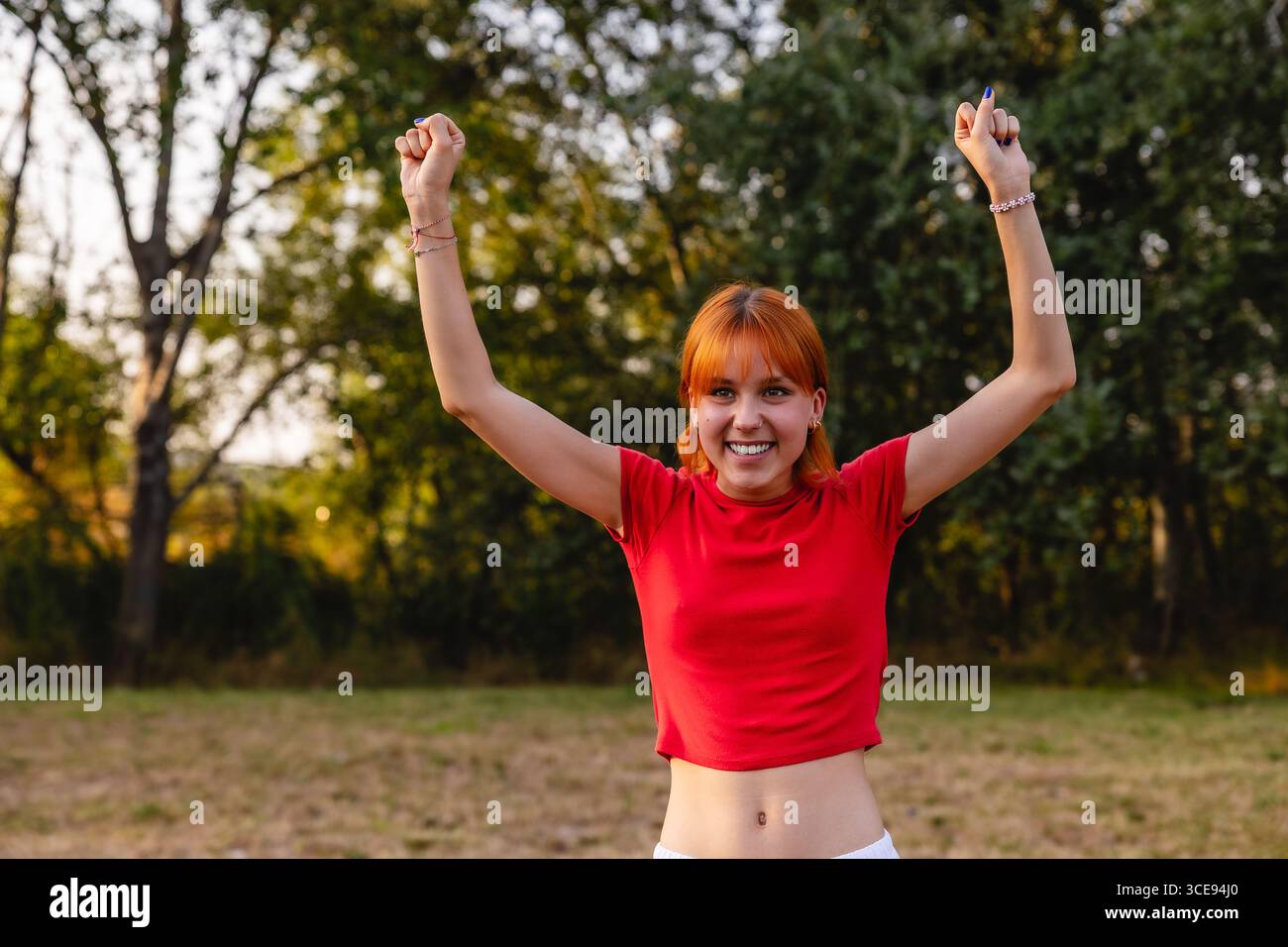 Young woman celebrating with raised arms in a park Stock Photo